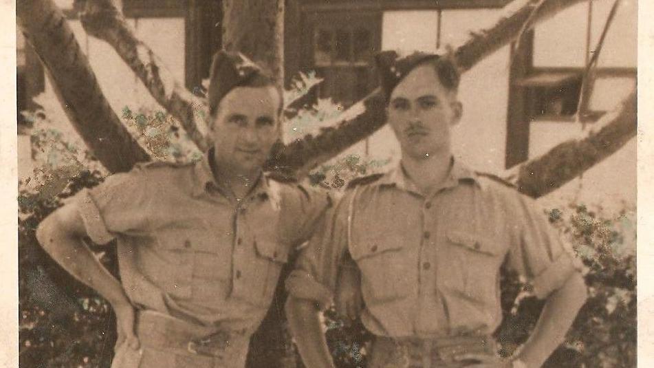 Joe Woods and a fellow solider in military uniform standing leant on a tree.