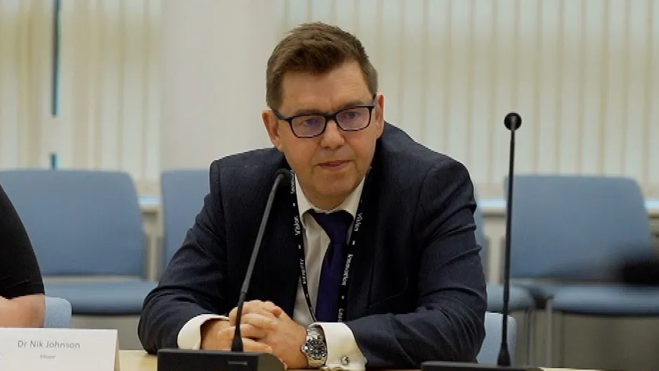 Dr Johnson wearing a black suit sitting in front of a microphone 