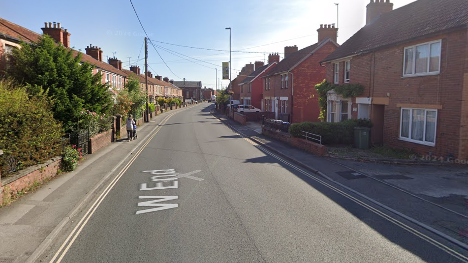 A road with houses on either side and cars passing in the distance.
