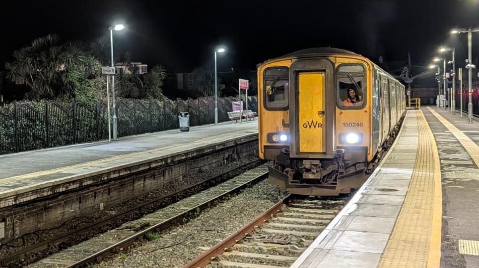 A wide shot of a Great Western Railway train pulling into the reopened Newqauy Station, at night.
