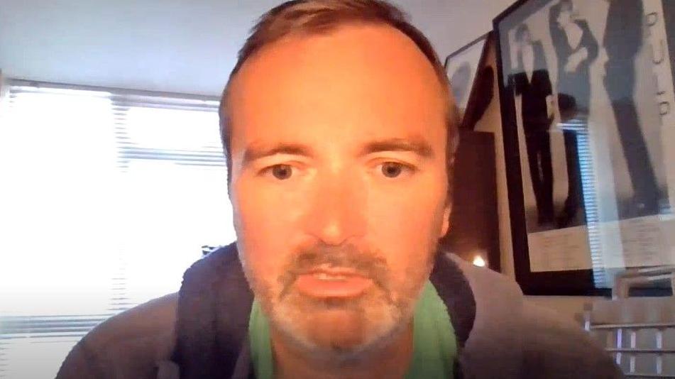 Chris Cook, 50, who has short brown hair and dark stubble, speaks into a camera during a video call