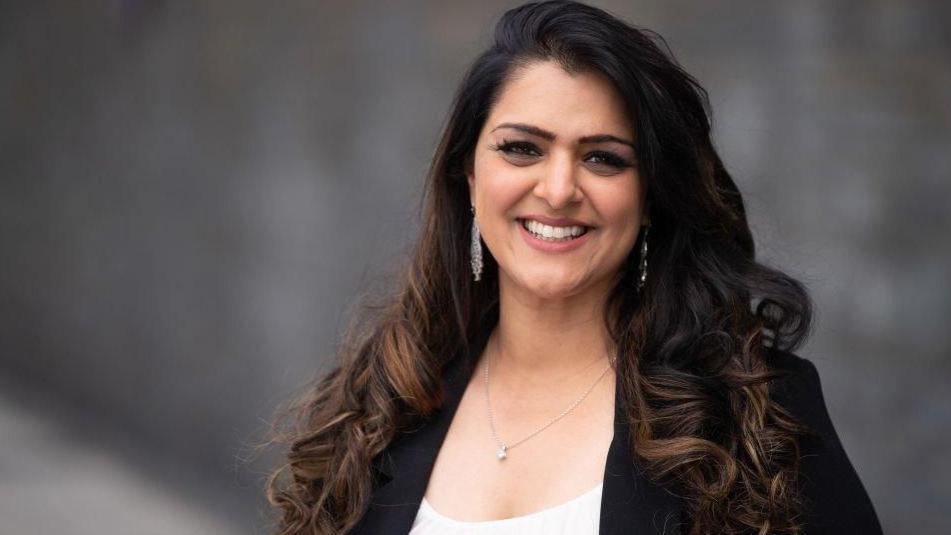 Natasha Asghar smiling to the camera with a blurred image of the wall of the Senedd building behind her