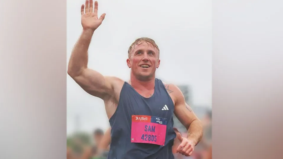 Sam Welleans during the Great North Run. He is wearing a running vest and has a hand raised in the air 