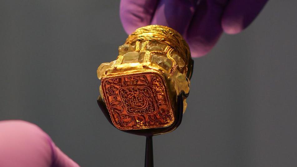 A person wearing purple gloves holds a gold piece of treasure