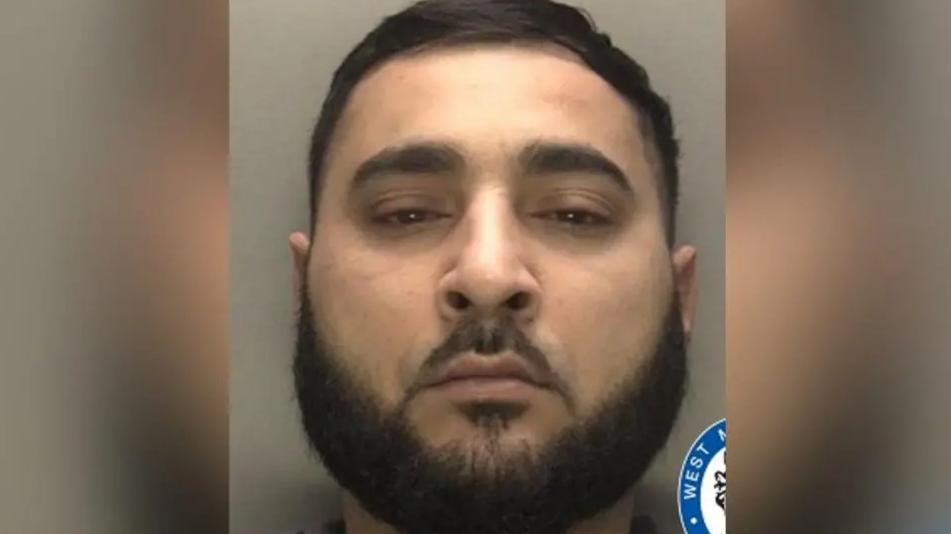 Mohammed appears in a police mugshot photo. He has dark hair and a beard and is staring directly at the camera.