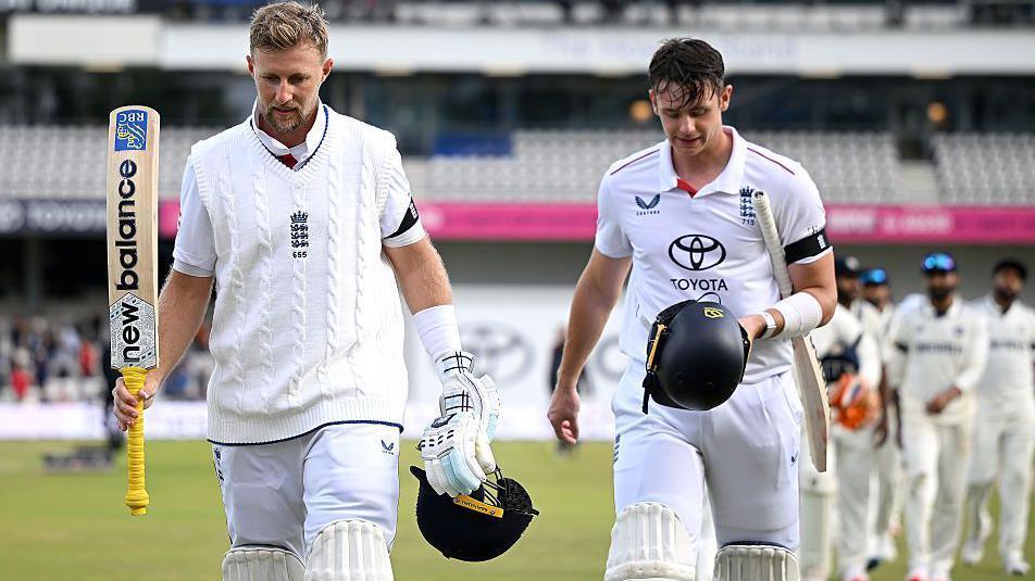 Joe Root, with the yellow handle on his bat, and Jamie Smith walk off heads bowed after leading England to victory against India. India's fielders are in the background