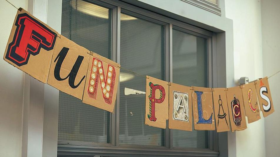 A cardboard sign strung across a window that says Fun Palaces, the individual letters display different fonts and colours