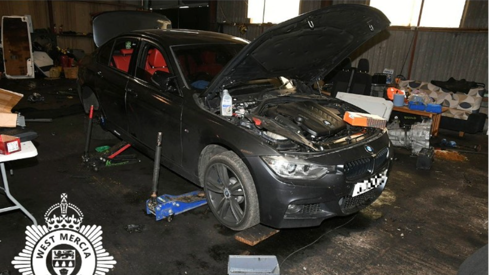 A black BMW car with the hood open while it is elevated off of the ground inside a garage