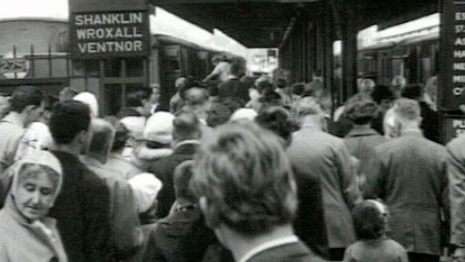 Holidaymakers waiting in a crowd at Ryde Pier Head station to board trains to resorts across the island in 1963 in a black and white image.