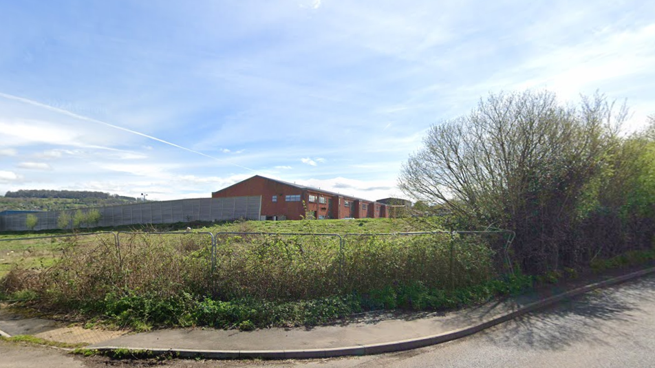 A brick industrial building surrounded by grassland and hedge rows 