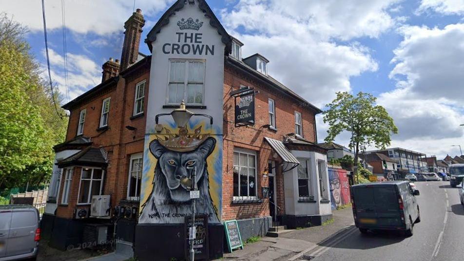 External shot of The Crown in Billericay. A mural of an animal wearing a crown is painted on one wall of the building, which sits on the corner of a road