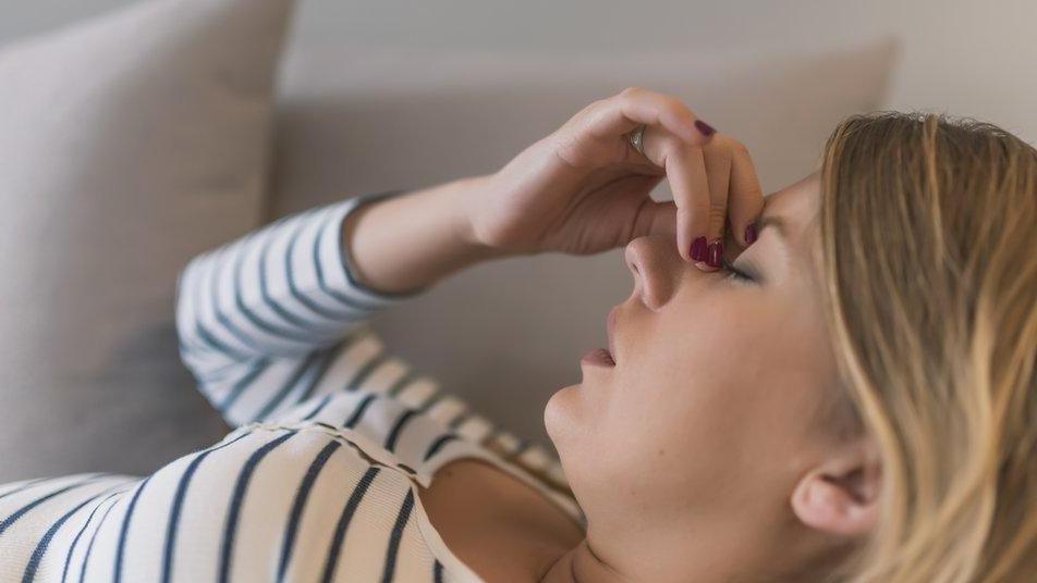 Close up of blonde woman lying on a couch holding the bridge of her nose with