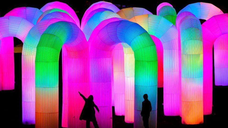 Silhouettes of two people amid brightly-coloured tubes - pinks and blues and oranges and greens.