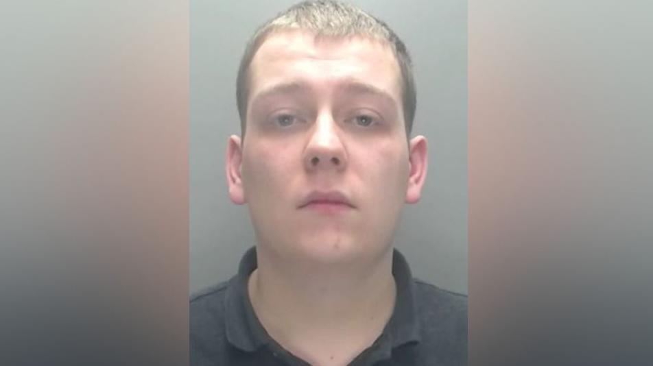 Mugshot of Thomas English. He is clean-shaven with short dark hair and is wearing a black polo shirt