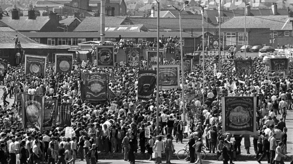 A black-and-white picture of a rally of striking miners, parading their banners, and their supporters, in Mansfield, Nottinghamshire, in May 1984.