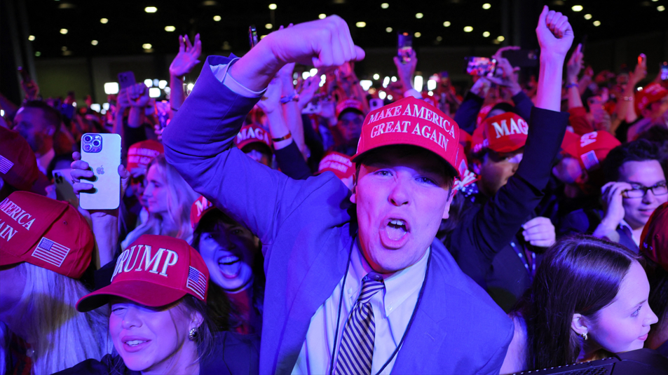 Trump supporters cheer while wearing campaign hats 