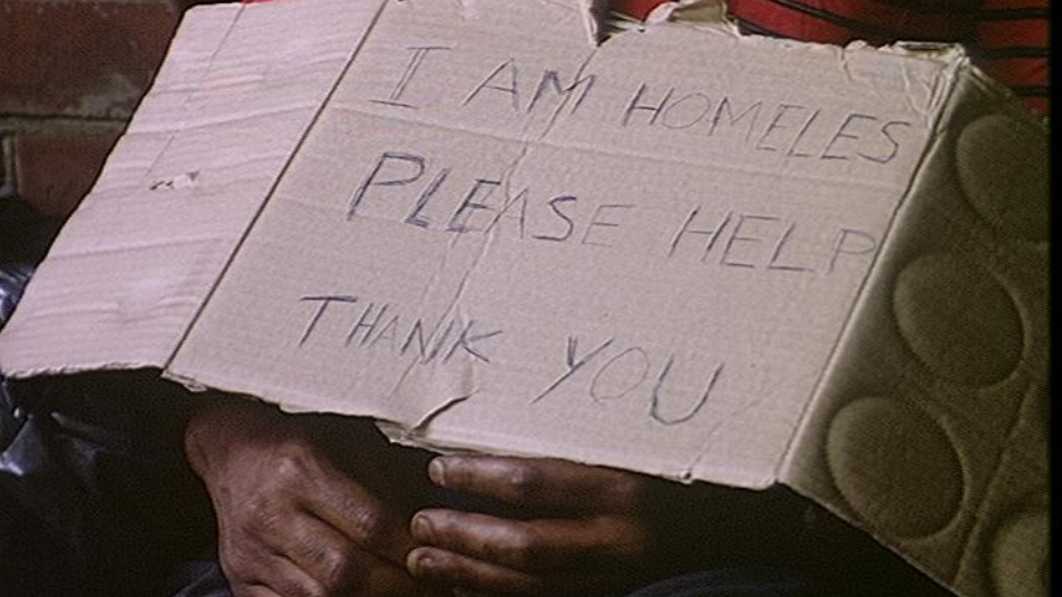 Homeless man with sign made out of cardboard which reads  'I am homeles. Please help. Thank you.' It is torn at the top and his hands are dirty with black fingernails.