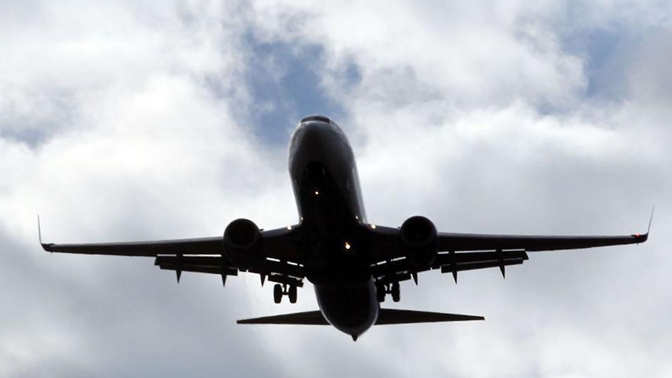 A passenger plane pictured in the sky in front of a cloudy sky