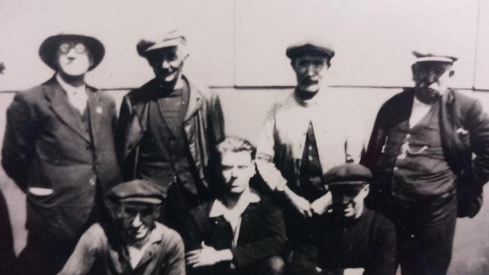 A black and white photo of the crew of the ship in the 1930s. Seven members, all wearing hats and waistcoats.