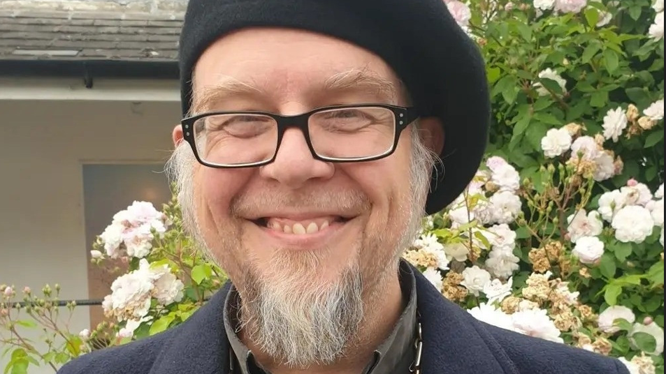 Jon Cousins smiling at the camera in front of flowers