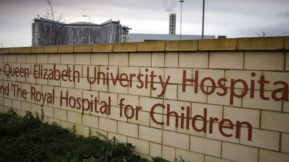 A sign on a wall says QEU University Hospital and royal Hospital for Children, with the hospital building behind it