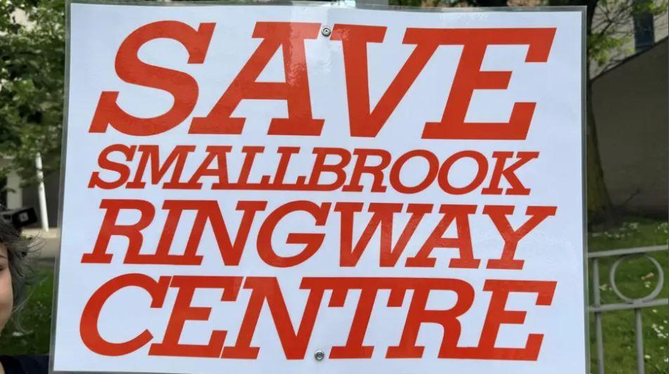 A white cardboard sign with bright orange text reading "save Smallbrook Ringway Centre"