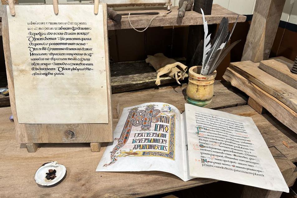 Parchment folios of an insular gospel book in progress with scribe’s tools on desk