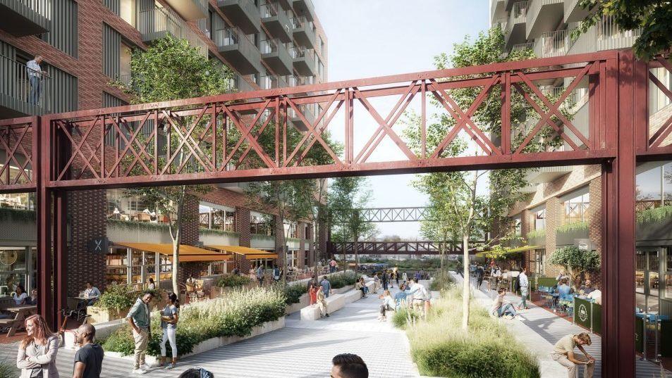 A computer generated image of how the development on Silverthorne Lane could look. It is an industrial style complex with corrugated metal walls and red metal bridges suspended above a large courtyard area, which has plant beds and benches. There are lots of people socialising in the courtyard, where there are restaurants and bars.
