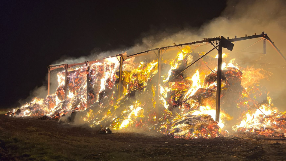 Bright orange flames and smoke can be seen rising from tall piles of material inside a burnt out frame of a building.