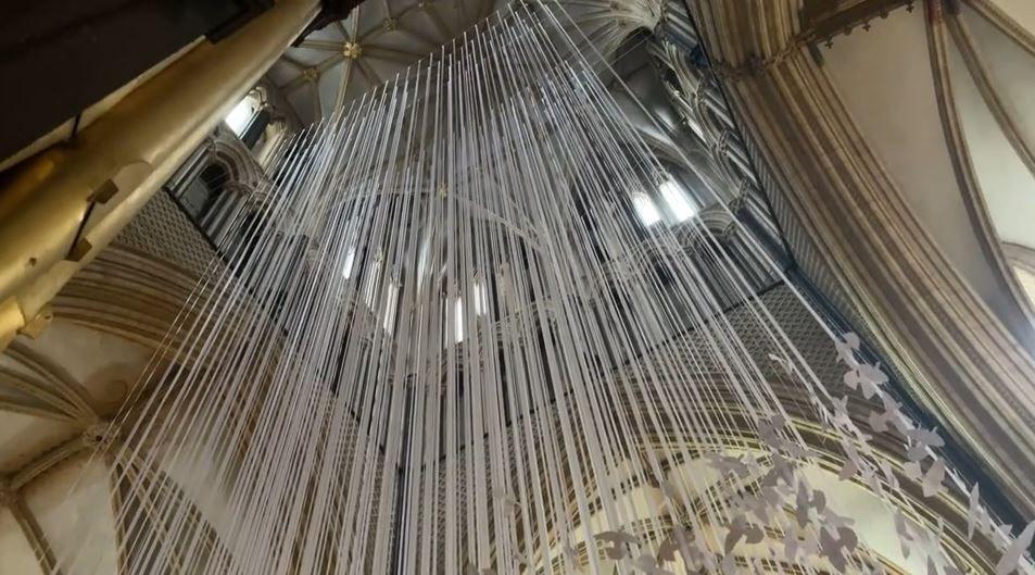 Hundreds of white cords suspended from the nave of the cathedral with the doves attached vertically at the bottom of each strand.