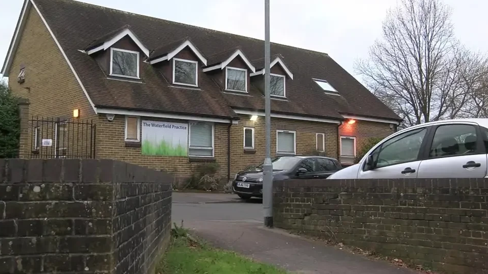 A general view of the Waterfield Practice in Bracknell, a two storey building with a sign saying "The Waterfield Practice" and two cars parked in its car park.