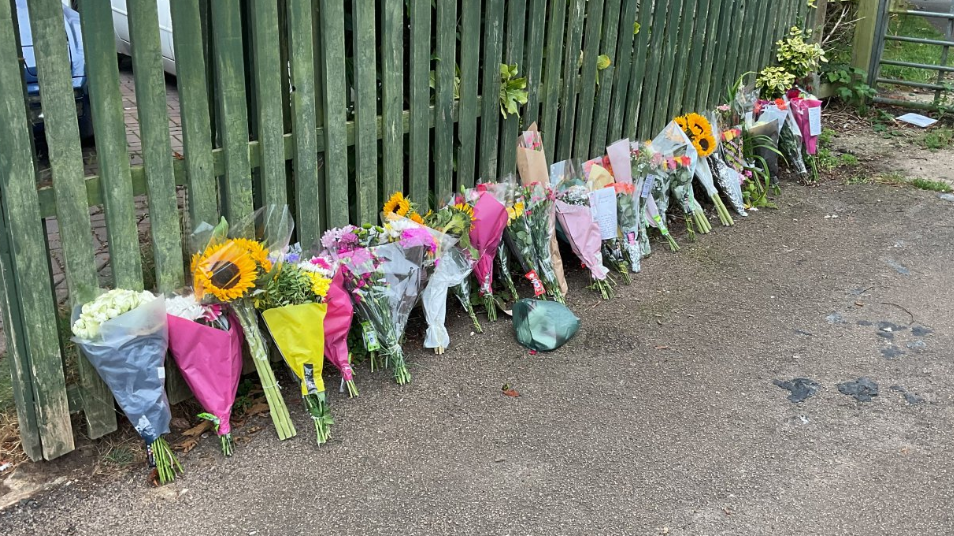 Bouquets of flowers leaning up against a green fence.