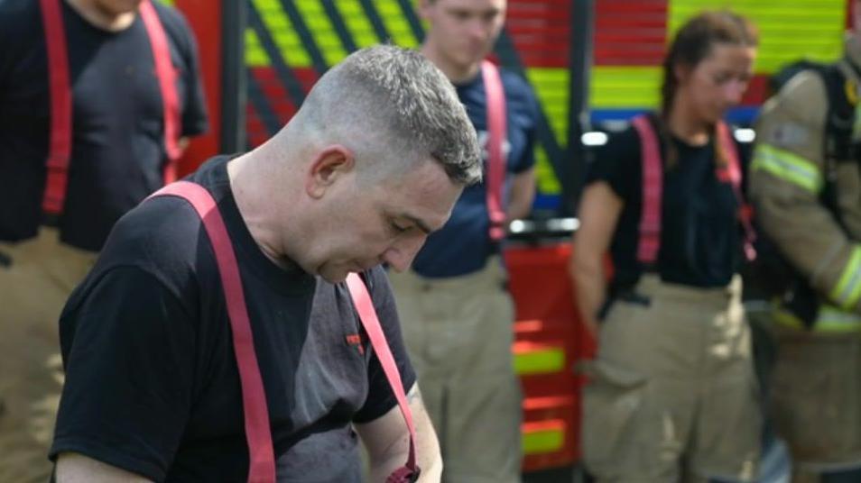 Jeremy observes a moments silence with colleagues in the background