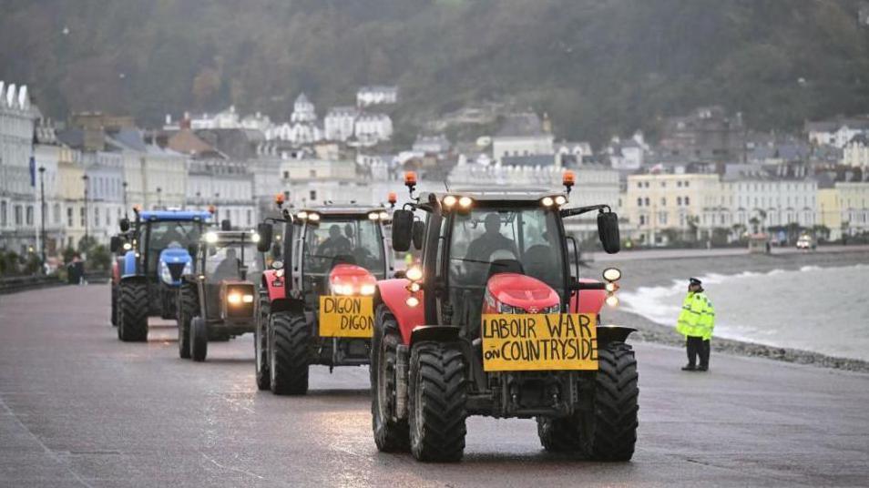 Four tractors on the promenade at Llandudno with a sign saying "Labour War on Countryside"