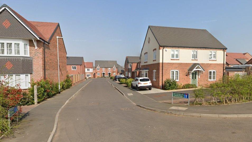 Several new-build houses on an estate with a road running through the middle and a road sign saying "Devereux Gardens". 