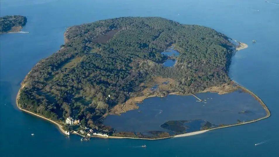 Areal view of Brownsea Island in Poole Harbour - a small island, mostly covered with trees and with a small number of houses and a lagoon closest to the camera