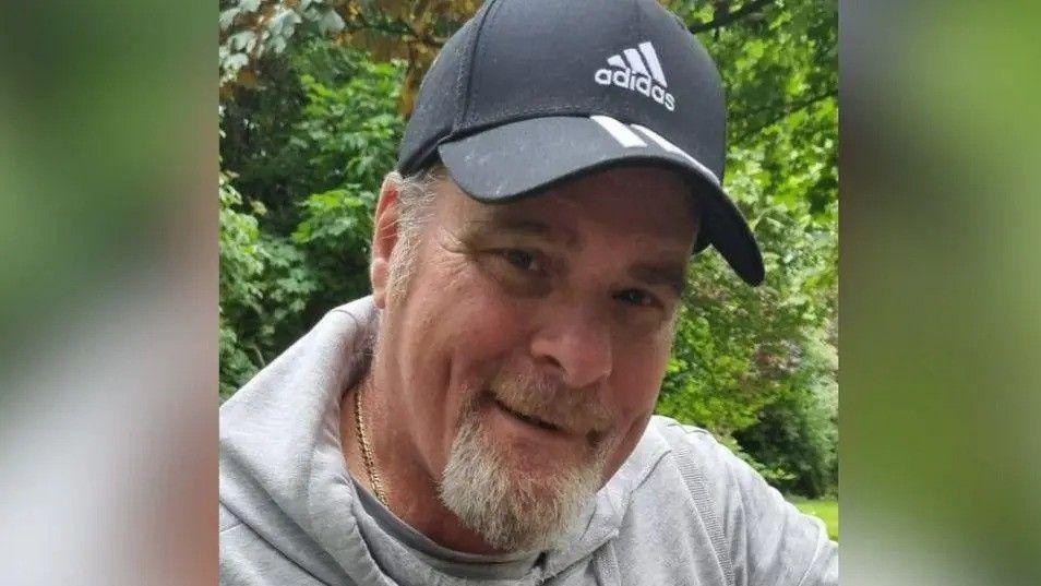 A man in his sixties with a goatee and a baseball cap. He is wearing a grey hoodie.