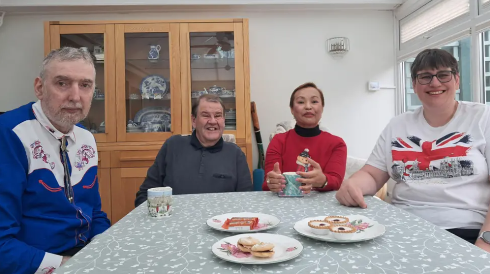 Four people sit around a dining table laden with biscuits and cups of tea.