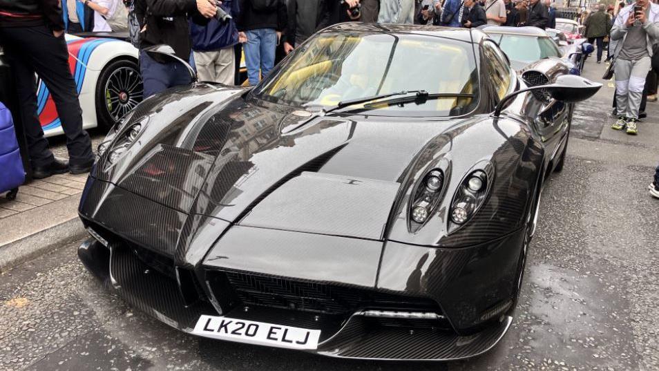 A Pagani Huayra Roadster, a black supercar with antenna-like wing mirrors, parked up on Pall Mall.