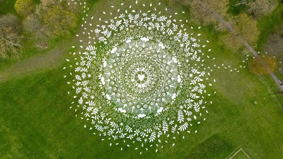 An aerial shot of the artwork etched in the lush green grass of the park. It is white, 80 metres in diameter and round, with the symbols radiating out.