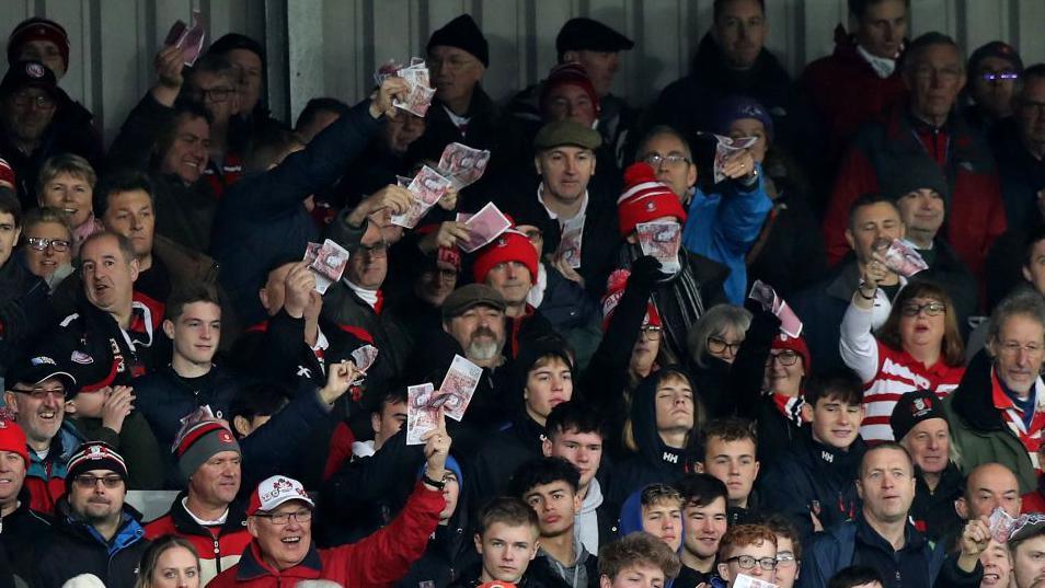 Gloucester fans wave fake money at Saracens players