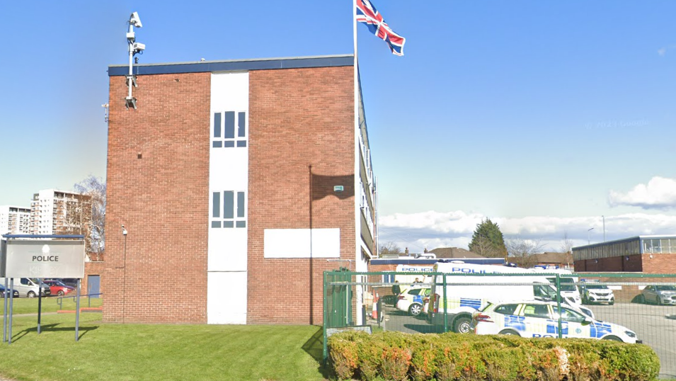 Kirkby police station in Kirkby, Merseyside. It is a three-storey brick building with a number of police cars and vans parked in its car park.