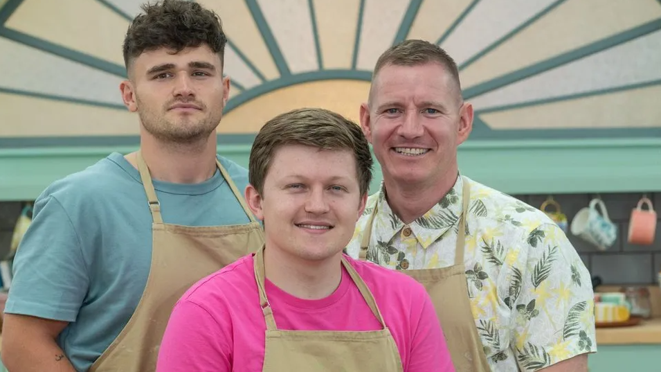 Matty Edgell in a blue T-shirt and beige apron standing with two other Bake Off contestants