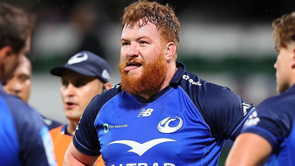 Harry Johnson-Holmes in blue Western Force shirt, looking slightly to left of frame with team-mates either side in foreground