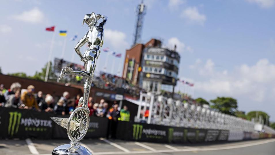 A close-up of a TT trophy, which features a silver figure wearing a winged helmet looking to the air above while balanced on a wheel and which has a wing.