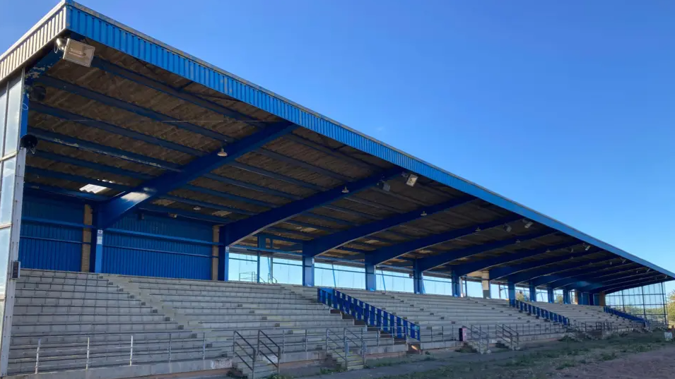 A blue and white grandstand with steps and silver railing and a blue roof