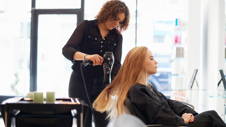 A hairdresser is drying her customer's long hair in a salon.