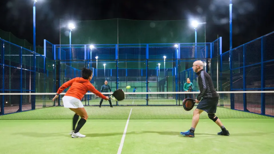 Four people play the game on a court. They are wearing different coloured sportswear and their rackets are black.