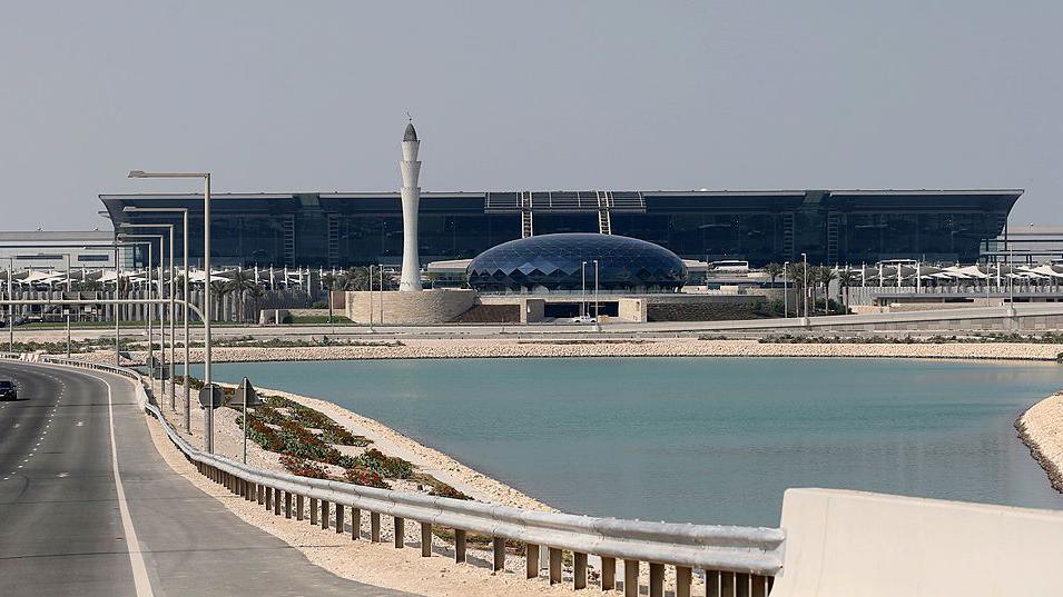 An exterior view of Doha's Hamad airport showing a lake in front of a terminal