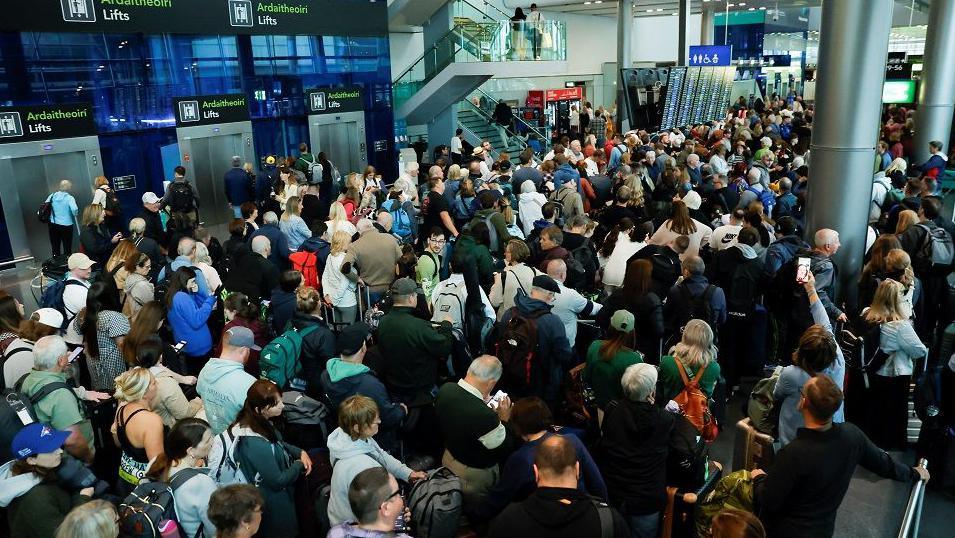 Queues of people inside Dublin Airport standing and waiting to be able to check in. 